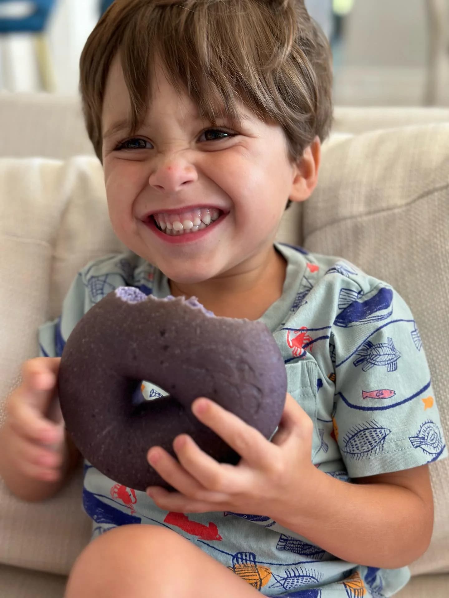 A young child joyfully biting into a purple rainbow bagel from Dan's Bagels